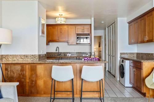 a kitchen with wooden cabinets and white stools at Oceanfront Condo with Heated Pool Hot Tub & Lanai in Wailuku