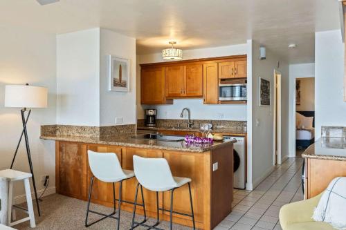 a kitchen with wooden cabinets and white stools at Oceanfront Condo with Heated Pool Hot Tub & Lanai in Wailuku