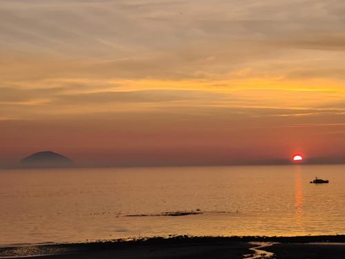 a sunset over the ocean with a boat in the water at Ailsa View in Girvan