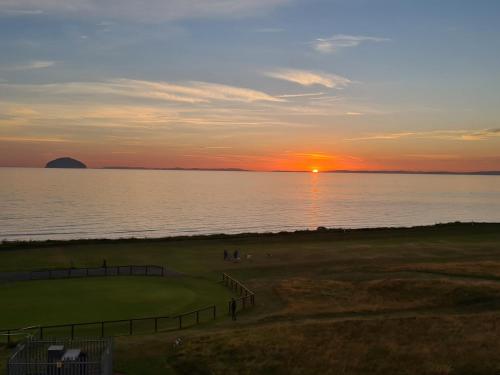 a sunset over a golf course with the ocean at Ailsa View in Girvan