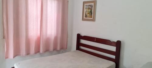 a bedroom with a chair and a pink curtain at Casa 30 metros da praia com wifi e garagem 6 carros in Praia Grande