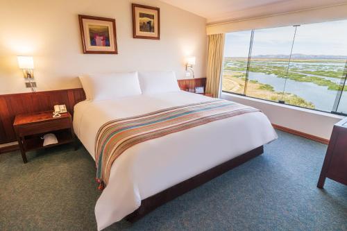 a large bed in a hotel room with a large window at GHL Hotel Lago Titicaca in Puno