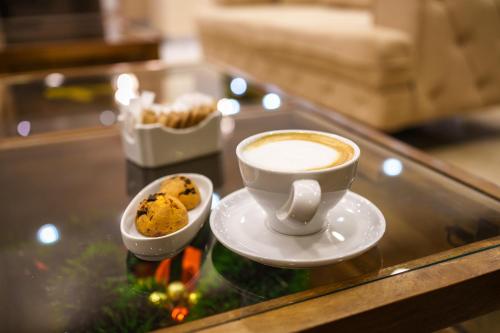 a cup of coffee and cookies on a glass table at Hotel Monogram Park in Ruma