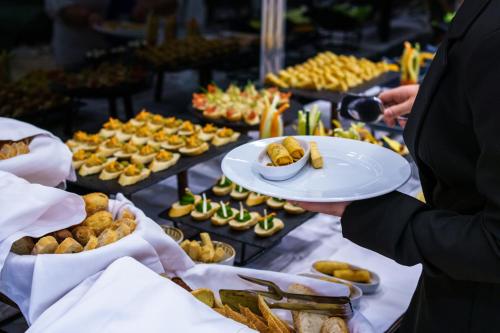 a person holding a plate of food at a buffet at Hotel Monogram Park in Ruma