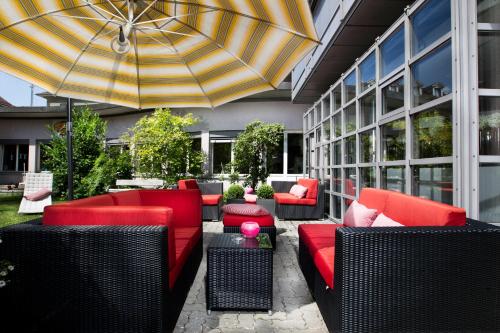 un patio con muebles rojos y sombrilla en Hotel La Pergola en Berna