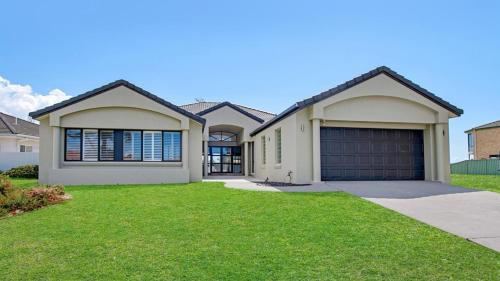 a large house with a garage in a yard at FLOATING ON THE CANALS - 80 COMMODORE CRES in Port Macquarie