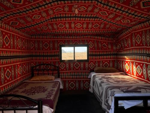 Cette chambre rouge comprend deux lits et une fenêtre. dans l'établissement wadi Rum Spirit of Peace Camp, à Wadi Rum