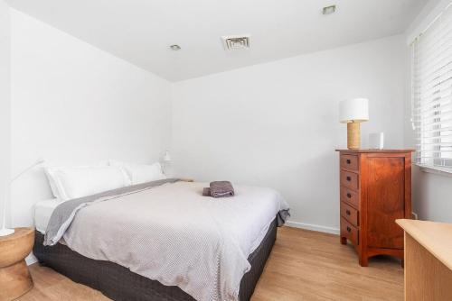 a white bedroom with a bed and a wooden dresser at Riverleigh, Gerroa in Gerroa