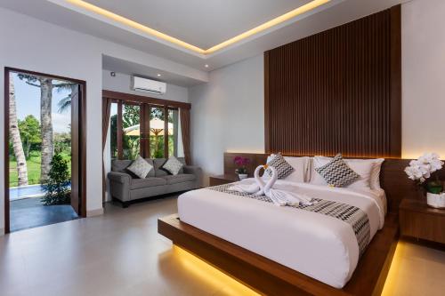 a bedroom with a large white bed and a couch at Pondok Deamore Villa in Gianyar