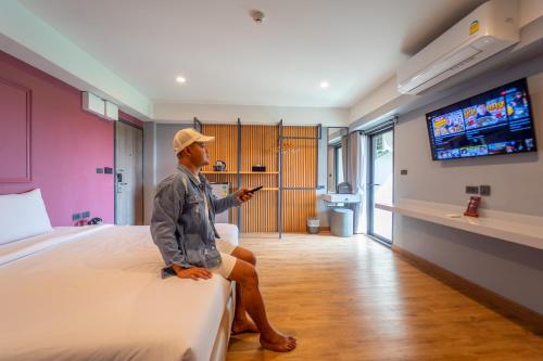 a man sitting on a bed in a hotel room at Lima Hotel in Phra Nakhon Si Ayutthaya