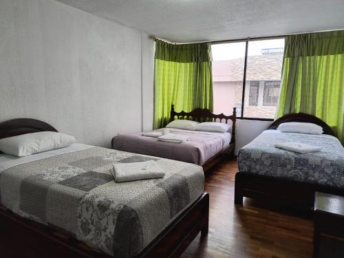 a bedroom with two beds and a window with green curtains at Hostal María - Otavalo in Otavalo