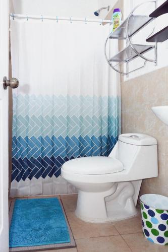 a bathroom with a white toilet and a blue shower curtain at La Petite Santa Ana in Santa Ana