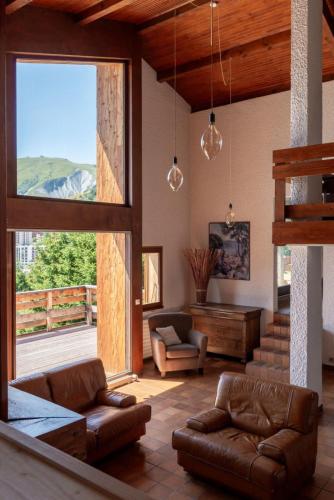 Elle comprend un salon doté d'un mobilier en cuir et d'une grande fenêtre. dans l'établissement Architect's Chalet with Stunning View - Close to Slopes and Shops, à La Toussuire