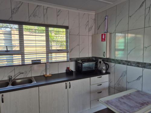une cuisine avec des armoires blanches, un évier et une fenêtre dans l'établissement Weaver's Corner Richards Bay, à Richards Bay