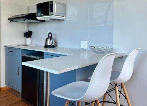 una cucina con due sedie bianche a un bancone di Casa Sí Apartment a Gqeberha