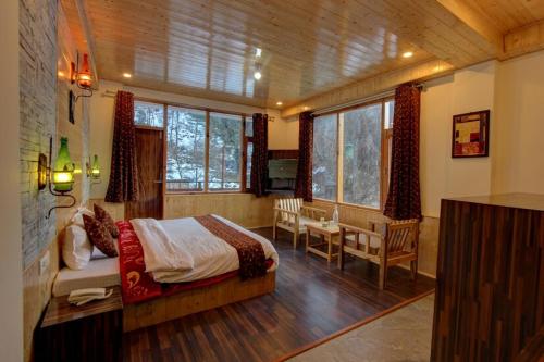 a bedroom with a bed and a desk and windows at Hotel 17 Miles Stone, Manali By Shivaneel Hospitality in Manāli