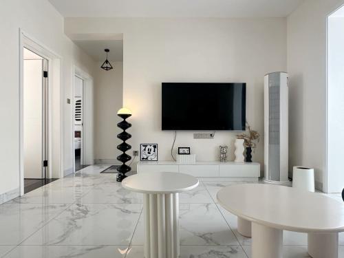 a white living room with a tv and a table at Island Flower Coconut 花椰椰民宿 in Haikou