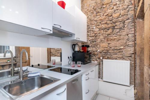 - une cuisine avec des placards blancs et un mur en pierre dans l'établissement Le Petit Mercière - Le charme en plein centre, à Lyon