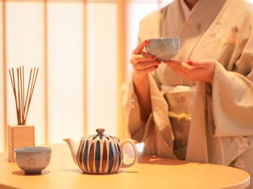 a woman is holding a cup on a table at 大日寺の宿 京都吉祥院 in Kyoto