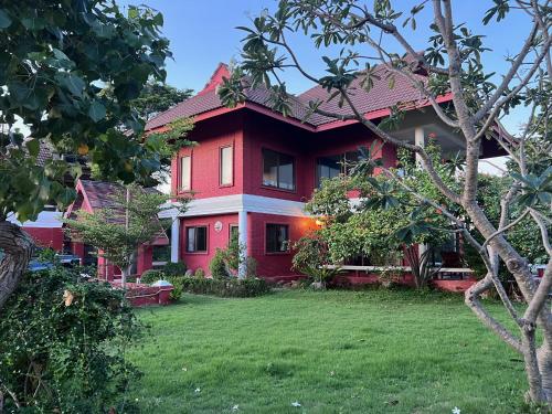 a red house with a lawn in front of it at Baan Plumeria บ้านภูมิเรีย in Phetchaburi