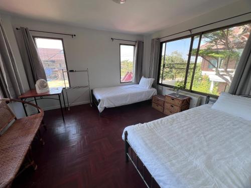 a bedroom with two beds and two windows at Baan Plumeria บ้านภูมิเรีย in Phetchaburi