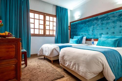 two beds in a room with blue curtains at Hotel Oudaya & Spa in Marrakech