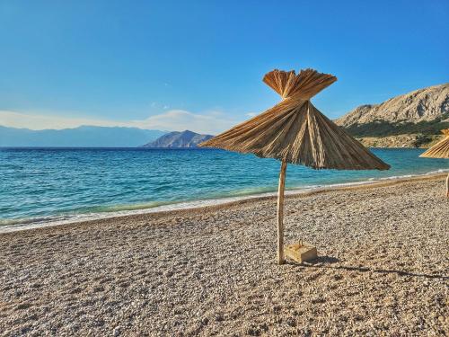 a beach with two straw umbrellas on the sand at Ferienhaus mit Meerblick & Pool in Baška - Villa-Planina in Baška