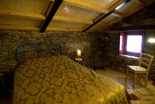 a bedroom with a bed in a stone room with a window at Palheiro do Castelo - Pátio in Sabugal
