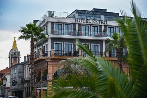 a hotel building with a clock tower and palm trees at Hotel Retro in Batumi