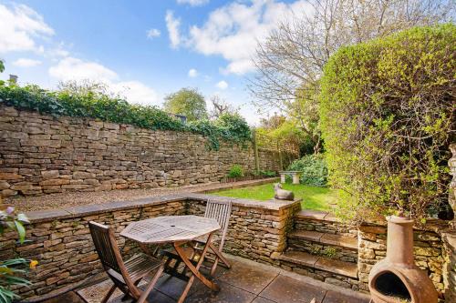 a table and chairs in a garden with a stone wall at Mouse Manor in Longborough