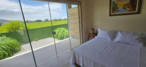 a bedroom with a bed and a large glass window at Hotel Barra da Ferrugem Eco Village in Garopaba