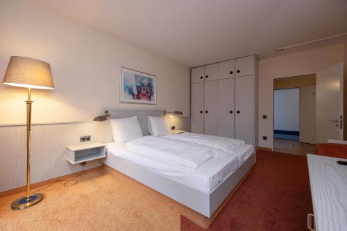 a large white bed in a room with a lamp at Fletcher Hotel-Restaurant Arnsberg-Sauerland in Arnsberg