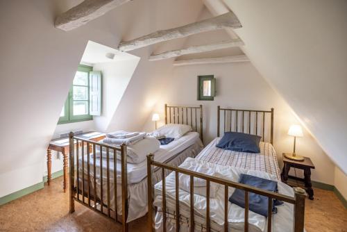 - 2 lits dans une chambre mansardée avec des murs blancs dans l'établissement Hameau de la Vidalie, à Thonac