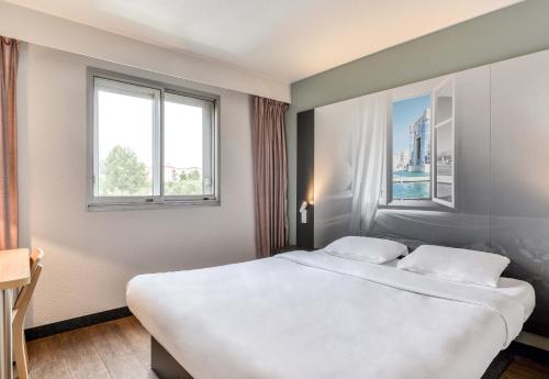 a bedroom with a large white bed with two windows at B&B HOTEL Montpellier Vendargues in Saint-Aunès