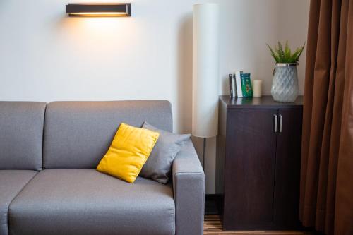 a gray couch with a yellow pillow sitting next to a cabinet at Clarion Aparthotel Toulouse Le Parc de l'Escale in Toulouse