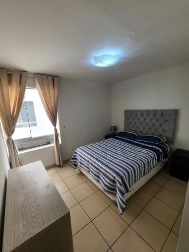 a bedroom with a bed with a striped comforter and a window at Departamento Centenario in Lima