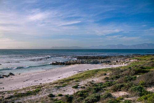 a beach with rocks and the ocean on a cloudy day at Luxury Beach House in Romansbaai Estate in Gansbaai