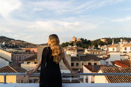 Eine Frau steht auf einem Balkon mit Blick auf eine Stadt in der Unterkunft Room Mate Leo, Granada in Granada