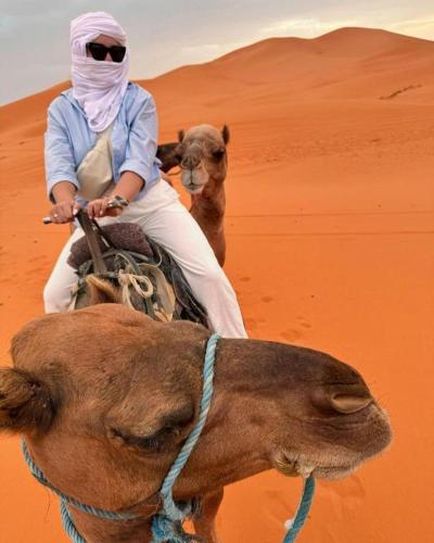 a woman riding a camel in the desert with a dog at Aladdin merzouga camp in Merzouga