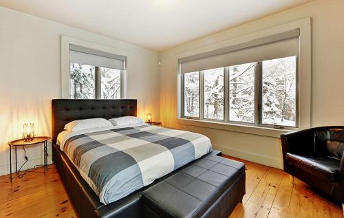 a bedroom with a bed and a couch and two windows at Chalets Alpins - 38 Chemin des Skieurs in Stoneham