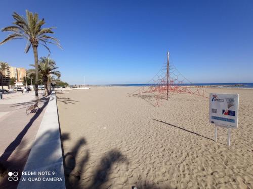 a beach with a sign in the sand and palm trees at Alice Home in Puebla de Farnals
