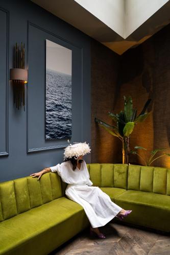 a woman sitting on a green couch looking at the ocean at Room Mate Collection Gorka, San Sebastián in Donostia-San Sebastián