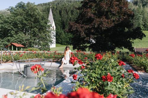 a woman sitting on a fountain in a garden with red flowers at Klostergut Kronburg in Zams