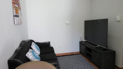 a living room with a black couch and a flat screen tv at Kombi Cove Blaauwberg in Cape Town
