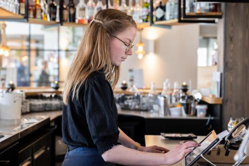 a woman standing at a bar using a laptop at Hotel De Walvisvaarder in Lies