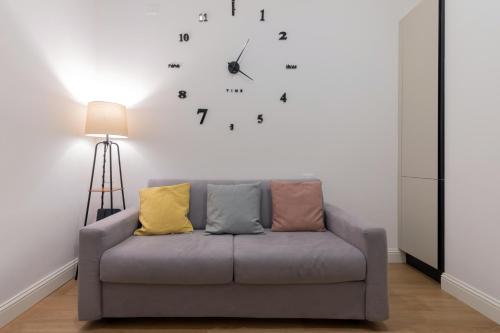 a couch in a living room with a clock on the wall at Casa Magenta a 4 minuti dalla metro WIFI & AC in Milan