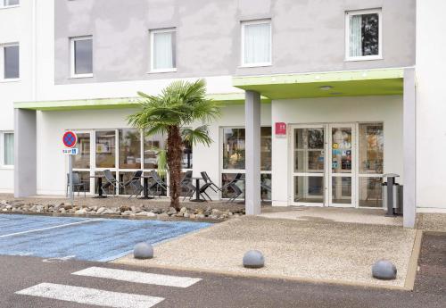 a white building with a palm tree in front of it at B&B HOTEL Mont-de-Marsan in Saint-Avit