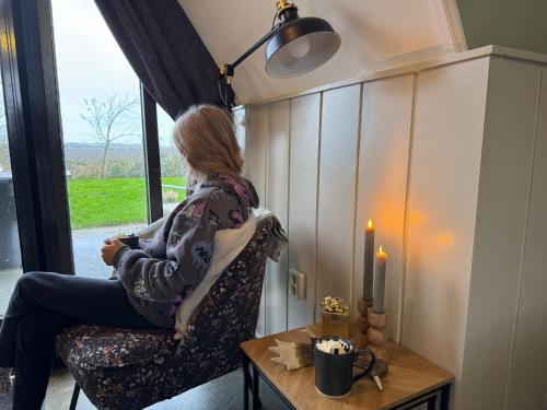 a woman sitting in a chair looking out a window at Hotelhuisjes Medemblik in Wieringerwerf