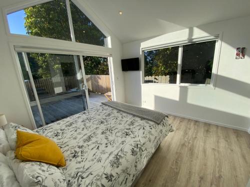 a bedroom with a bed and two large windows at Maraetai -Kererū Cottage - Whole House in Maraetai