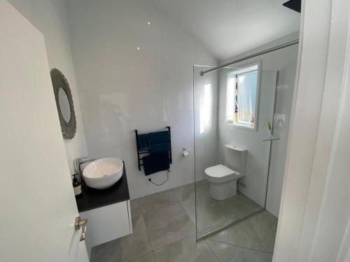 a white bathroom with a sink and a toilet at Maraetai -Kererū Cottage - Whole House in Maraetai